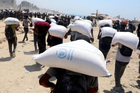 Palestinos carregam sacos de farinha após a entrada de ajuda humanitária em Gaza por um ponto de passagem na fronteira, em Beit Lahia, no norte da Faixa de Gaza, em 27 de julho de 2025. Foto: Rizek Abdeljawad/Xinhua